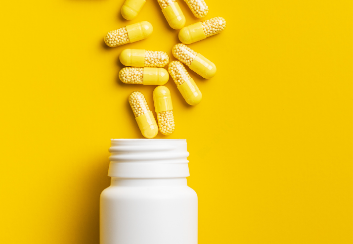 Bottle with Capsules Spilling Out on Yellow Background