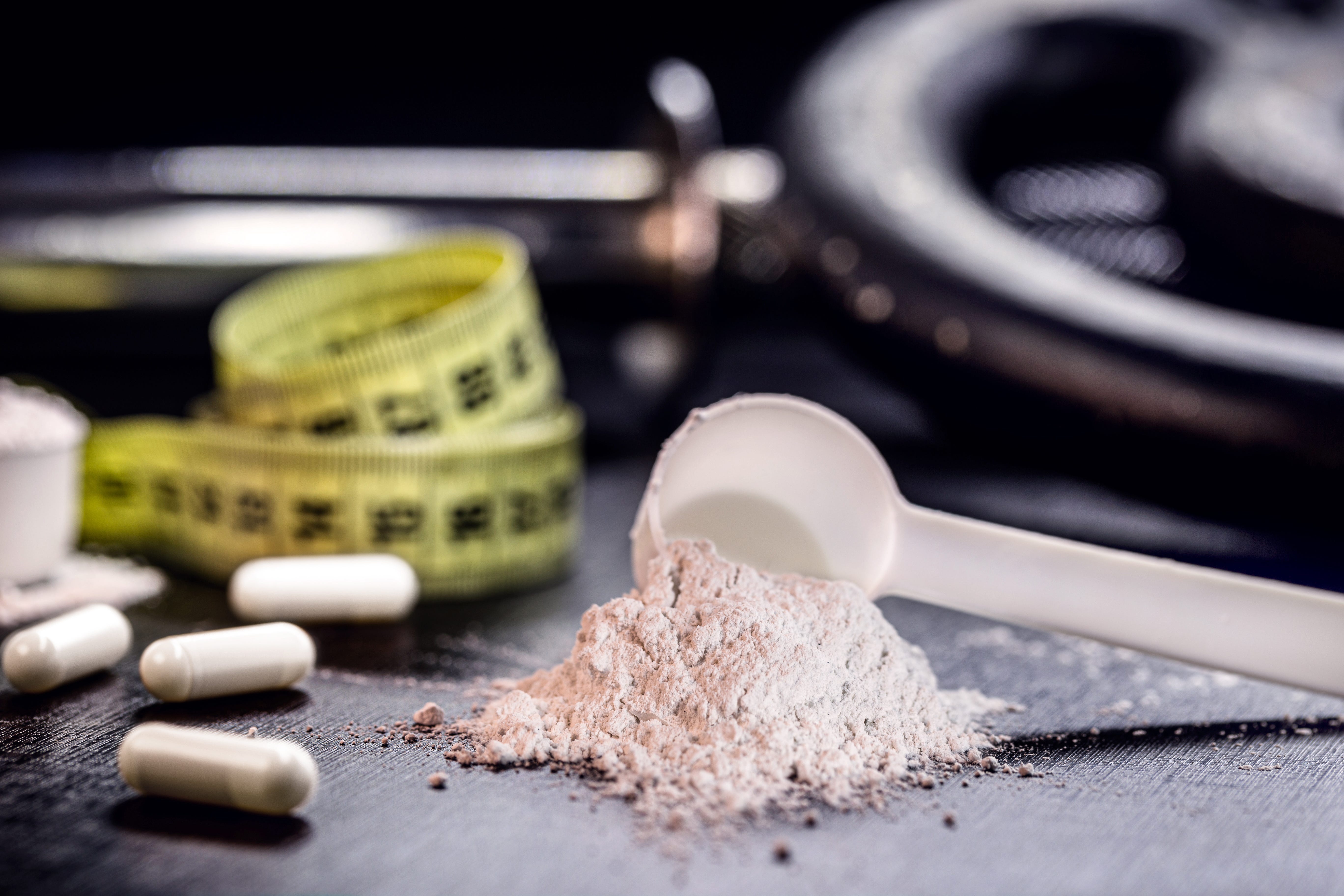 Creatine powder and capsules next to a dumbbell